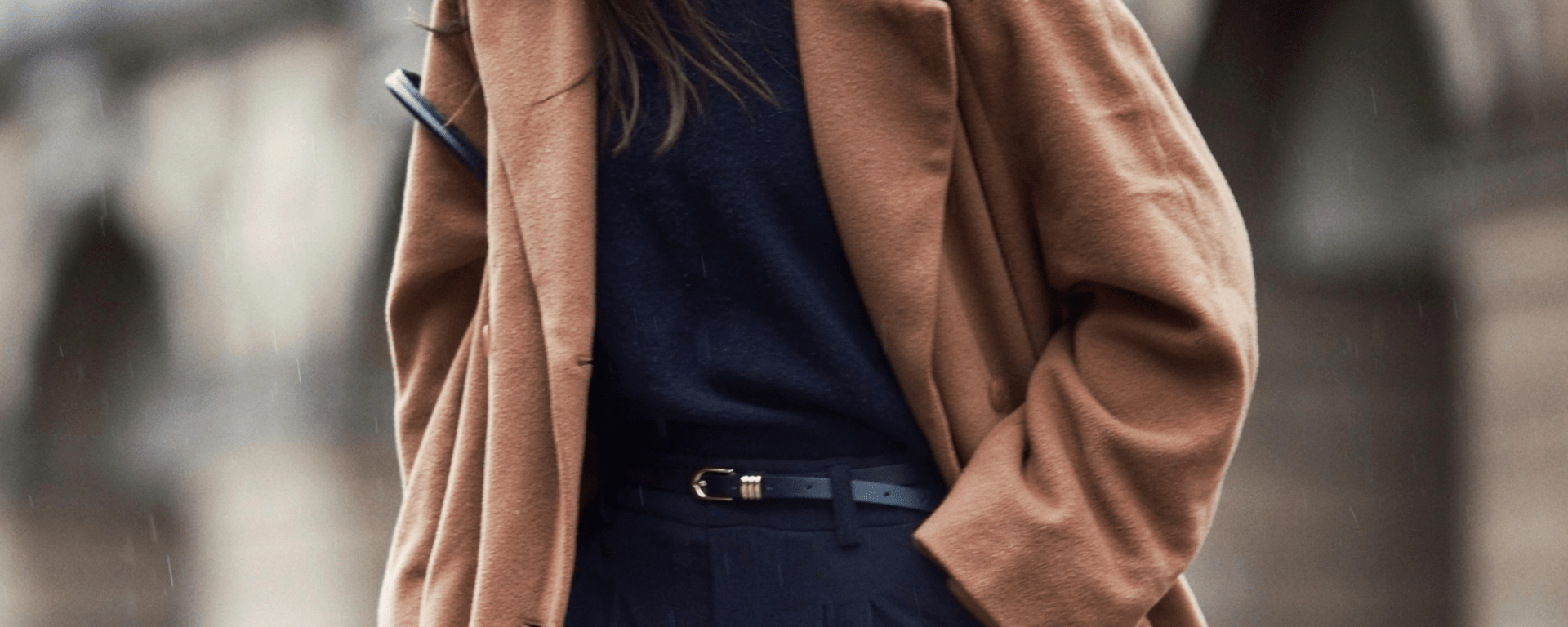 A woman wearing a camel winter coat and black trousers